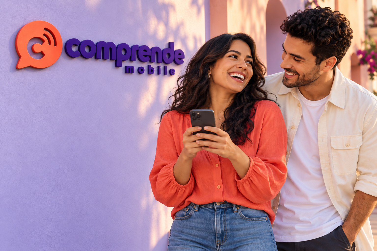 Two friends laughing together outside a lavender wall with a Comprende Mobile sign, one of them holding a phone.
